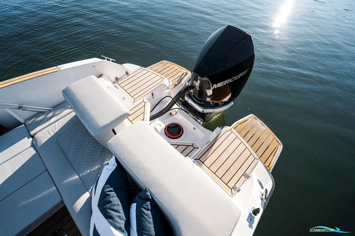Luxury boat deck featuring plush grey seating, a Mercury motor, wooden accents, and calm water under bright sunlight.